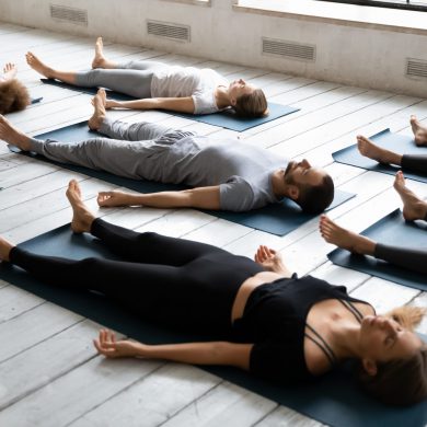 Young people meditating in Savasana pose, practicing yoga at lesson Young sporty people with closed eyes meditating in Savasana pose on floor, practicing yoga at group lesson, doing Corpse exercise on mats, training, working out in modern yoga studio, center
